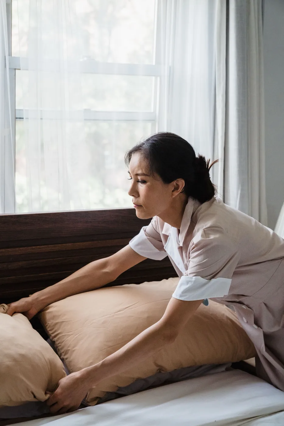A house cleaning pro making a bed in a sunlit bedroom, booked through SnipeTask