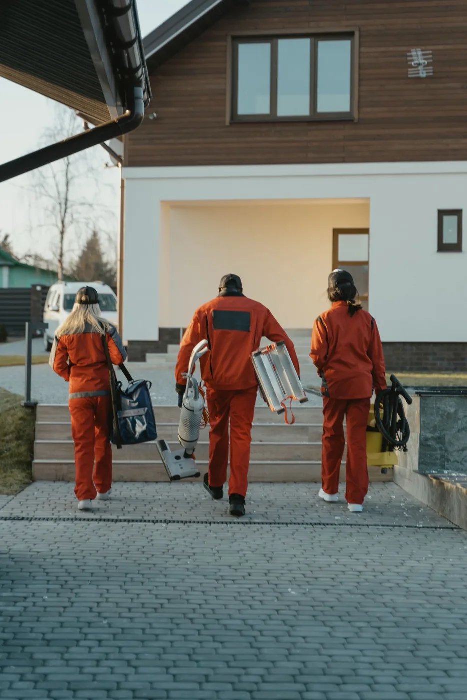 A three-person moving crew carrying equipment up to a house
